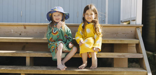 Two young children in colorful waterproof rainwear sitting on wooden steps outdoors