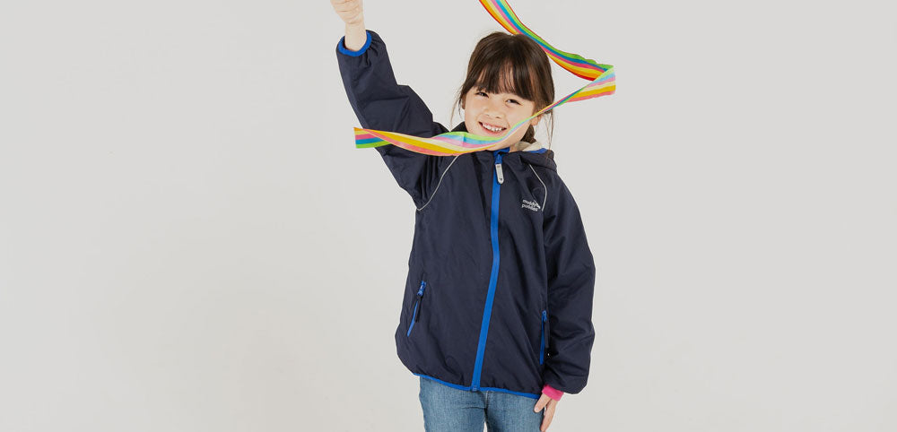 Smiling child in a navy waterproof jacket playing indoors with a colorful ribbon