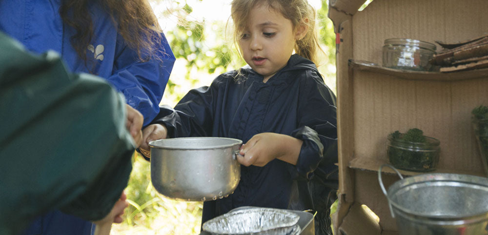 Child in waterproof jacket playing outdoors with pots and natural materials