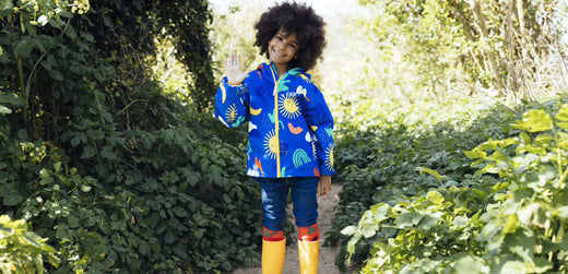 Child in colorful waterproof jacket and yellow rain boots outdoors on a leafy path