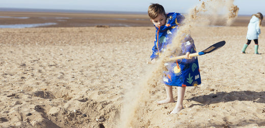 Child in waterproof raincoat playing on sandy beach, digging with a spade