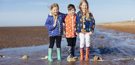 Children wearing colorful waterproof jackets and rain boots playing by the beach
