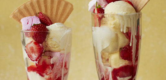Two tall glasses filled with strawberry ice cream sundaes, fresh berries, wafers, and marshmallows.