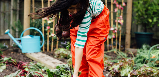 Child gardening outdoors in orange waterproof trousers and striped top