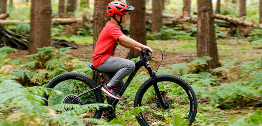 Child in outdoor clothing riding a mountain bike through a forest trail.