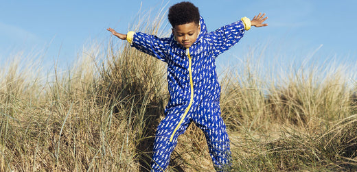 Child wearing blue waterproof rain suit playing outdoors in grassy sand dunes