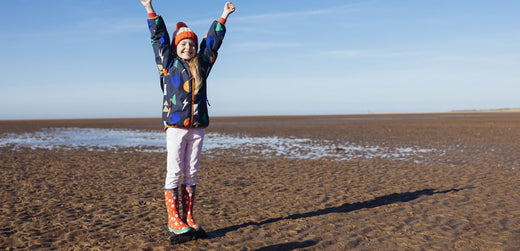 Child in waterproof jacket and red wellies smiling on a sandy beach outdoors