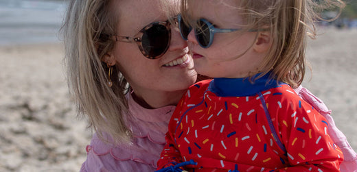 Adult and child wearing sunglasses at beach, child in red waterproof jacket with colorful print
