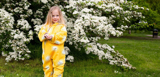 Child in yellow waterproof rain suit standing outdoors by flowering bush