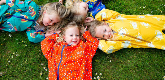 Children in colorful waterproof raincoats lying on grass, outdoor kids rainwear