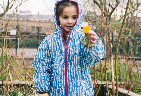 girl stood in garden holding a flower, wearing vibrant blue muddy puddles raincoat