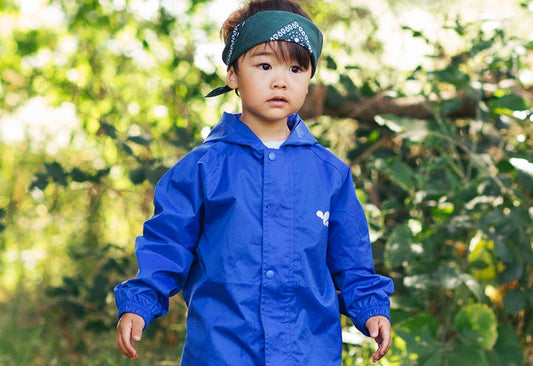 boy standing in front of tree wearing vibrant blue waterproof jacket and green bandana