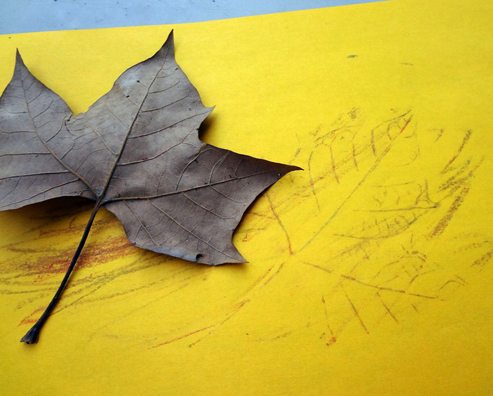 dried autumn leaf on a yellow piece of paper being used for wax rubbings