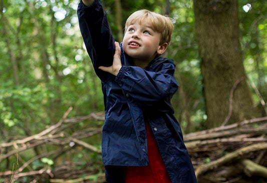 boy stood in woodland area pointing at something in the treetops, wearing navy muddy puddles waterproof jacket