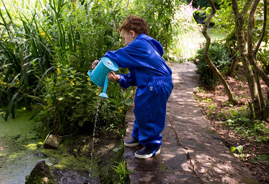 toddler boy emptying a blue watering can into a pond, wearing bright blue muddy puddles puddlesuit