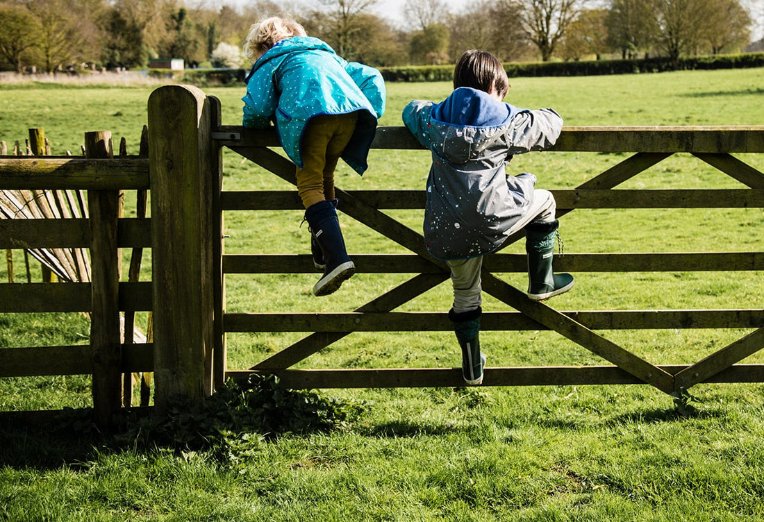 children climbing over a fence in a field, wearing vibrant muddy puddles raincoats and wellies