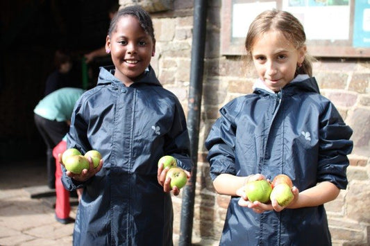 school children wearing navy muddle puddles raincoats, holding farm grown apples