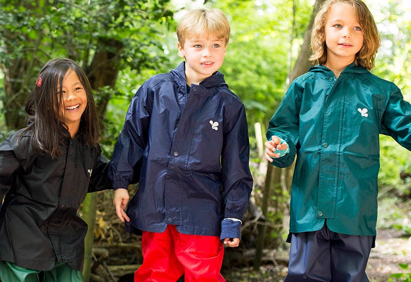 children standing in forest clearing wearing colourful muddy puddles waterproof jackets and trousers