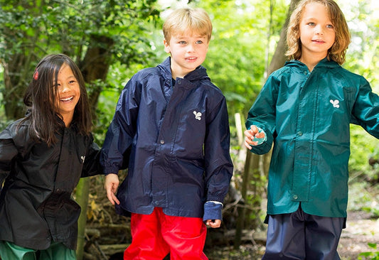 children standing in forest clearing wearing colourful muddy puddles waterproof jackets and trousers
