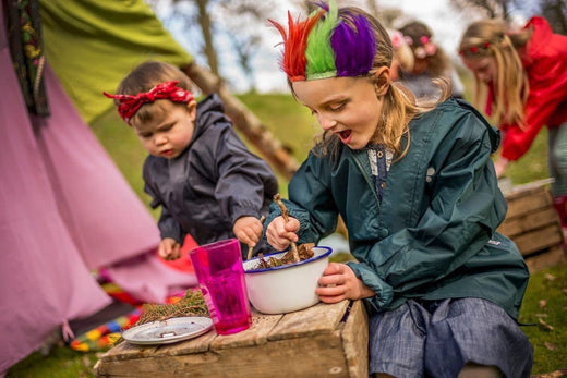 children at forest school setting wearing colourful headwear and muddy puddles waterproofs