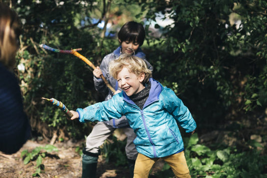 children laughing and playing with long sticks, wearing vibrant muddy puddles waterproofs