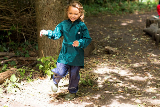 child running through woodland area wearing green muddy puddles waterproof jacket and navy trousers
