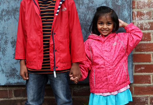 children holding hands in front of brick wall wearing colourful pink and red muddy puddles raincoats