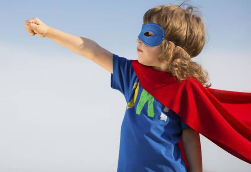 boy wearing a blue mask and red cape, doing a superman pose