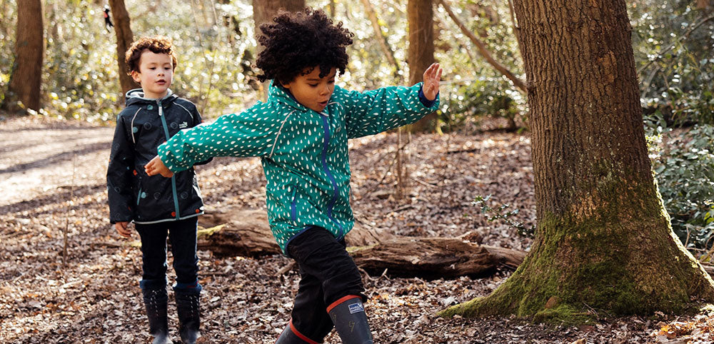 Children wearing waterproof jackets and boots playing outdoors in a woodland setting