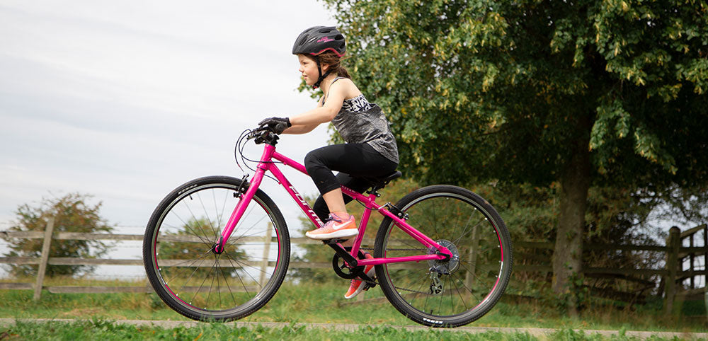 Child riding pink bicycle outdoors in waterproof clothing and helmet
