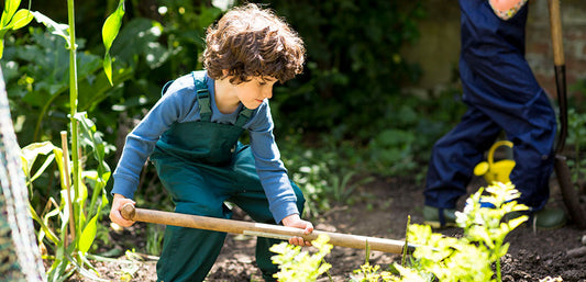 boy doing gardening with spade, wearing muddy puddles green waterproof dungarees and long sleeved blue top