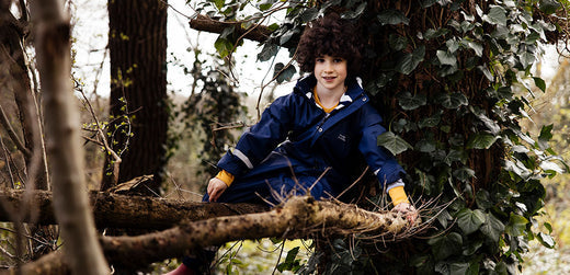 boy sitting on tree branch, wearing navy muddy puddles waterproof jacket and trousers