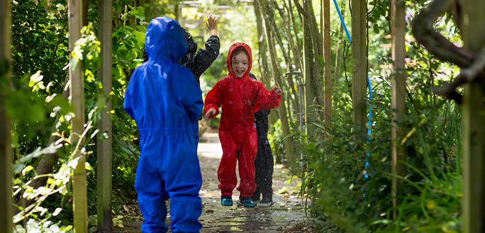 children wearing vibrant muddy puddles puddlesuits in the rain