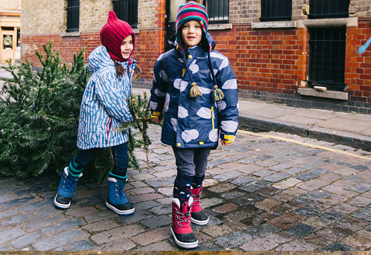 children pulling christmas tree along, wearing vibrant muddy puddles ski jackets and wellies