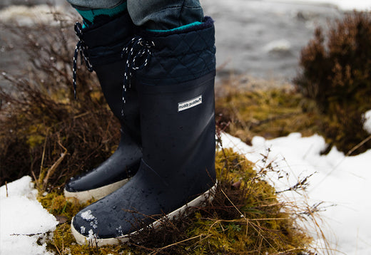 child wearing navy fleece lined drawstring wellies on a snowy grassy mound