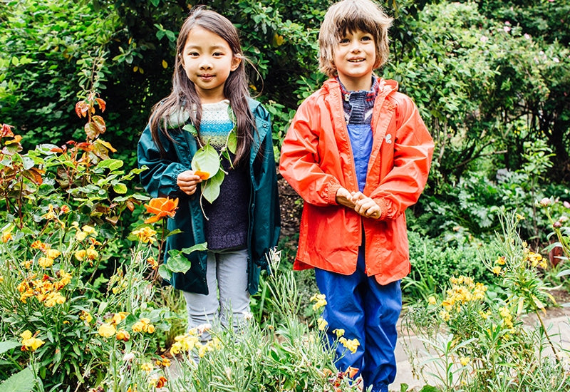 boy and girl stood in garden, wearing vibrant muddy puddles waterproof jackets and waterproof trousers
