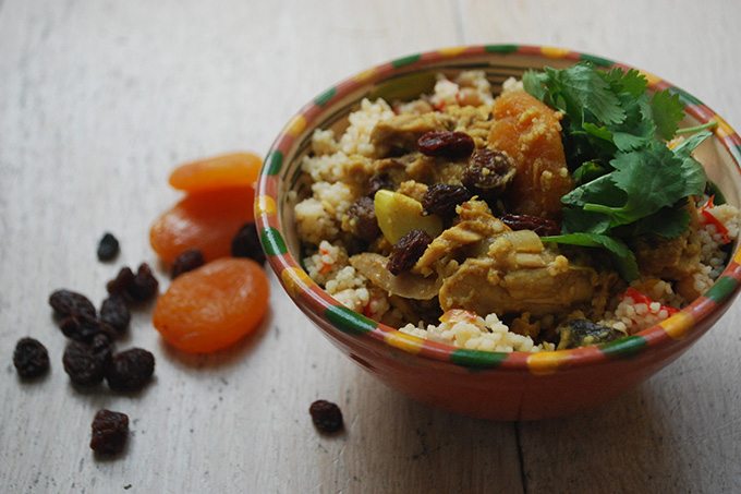 chicken almond and apricot tagine in a stoneware bowl, next to a pile of dried apricots and raisins