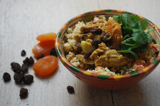 chicken almond and apricot tagine in a stoneware bowl, next to a pile of dried apricots and raisins