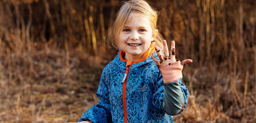 Smiling child outdoors in blue patterned waterproof jacket showing muddy hand