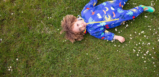 Child wearing colorful waterproof rain suit lying on green grass outdoors