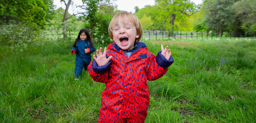 Smiling children in waterproof rain suits playing outdoors in a green grassy field