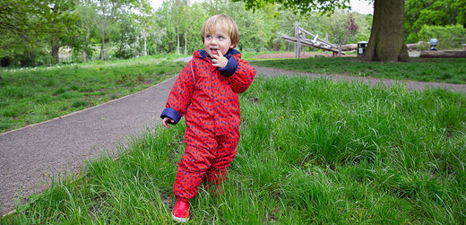 Young child in red waterproof rain suit standing on grass in outdoor park