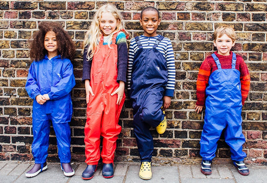 children stood in front of brick wall wearing blue and red muddy puddles waterproofs