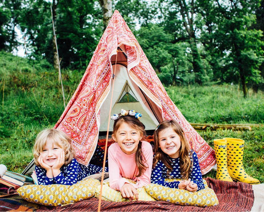 girls laying down in front of a teepee, wearing vibrant blue muddy puddles thermals