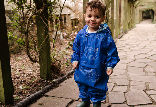 boy standing on garden path wearing a blue patterned muddy puddles puddlesuit