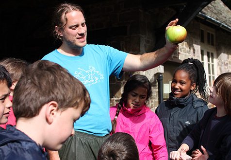 farms for city children adult leader speaking to a group of children, and holding a green apple