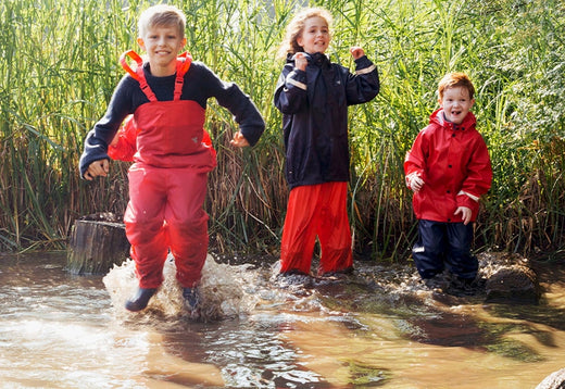 children jumping in muddy puddle wearing red and navy muddy puddles waterproofs