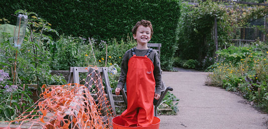 boy standing in allotment wearing red muddy puddles waterproof dungarees