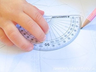 child drawing around a maths protractor with a pink pencil