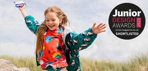 Smiling girl outdoors wearing colorful children's waterproof jacket and rainwear, grassy background